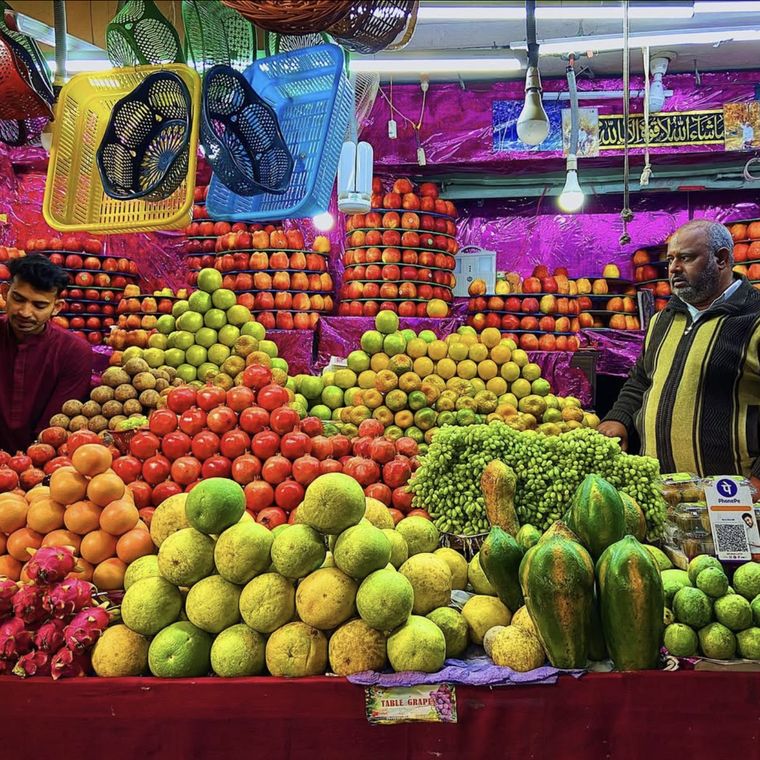 Fruit vendors behind a stacked display, a payments QR code on the counter
