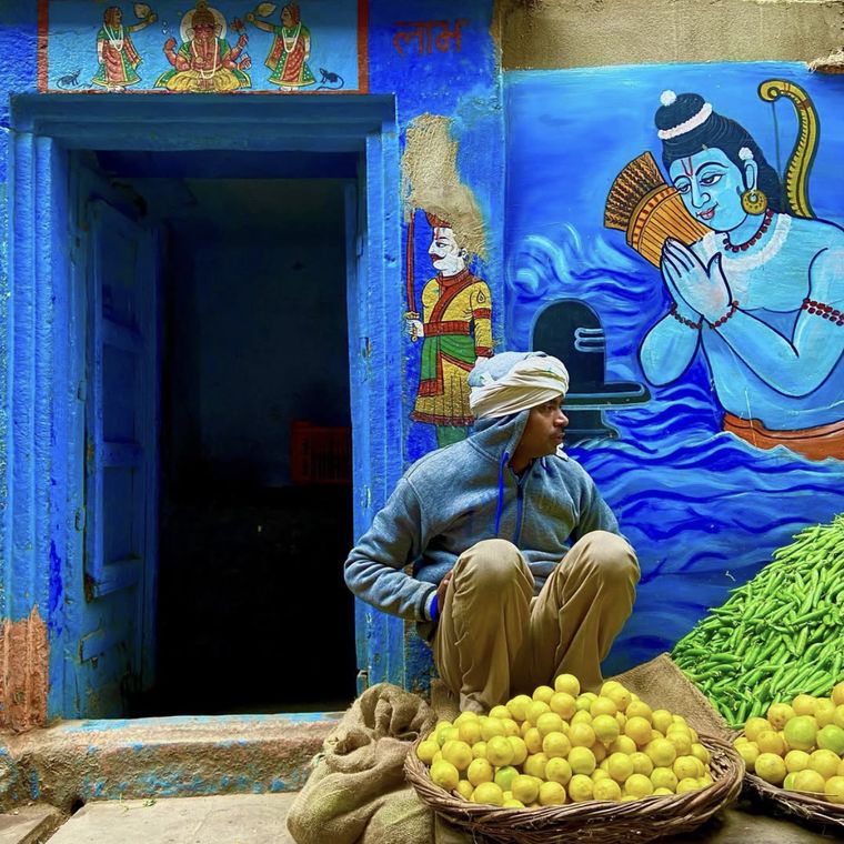 A vendor seated with baskets of lemons beside a painted wall